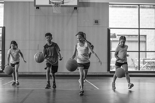 elementary school physical education students dribbling balls in a school gymnasium
